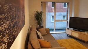 A modern living room with a sofa, a television, and a large window. - Stylish 2-bed Apartment in Manchester City Center (Manchester)