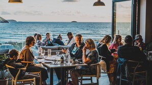 A group of people seated around a table in a room with a view of the sea. - Polzeath Beach House (Wadebridge)