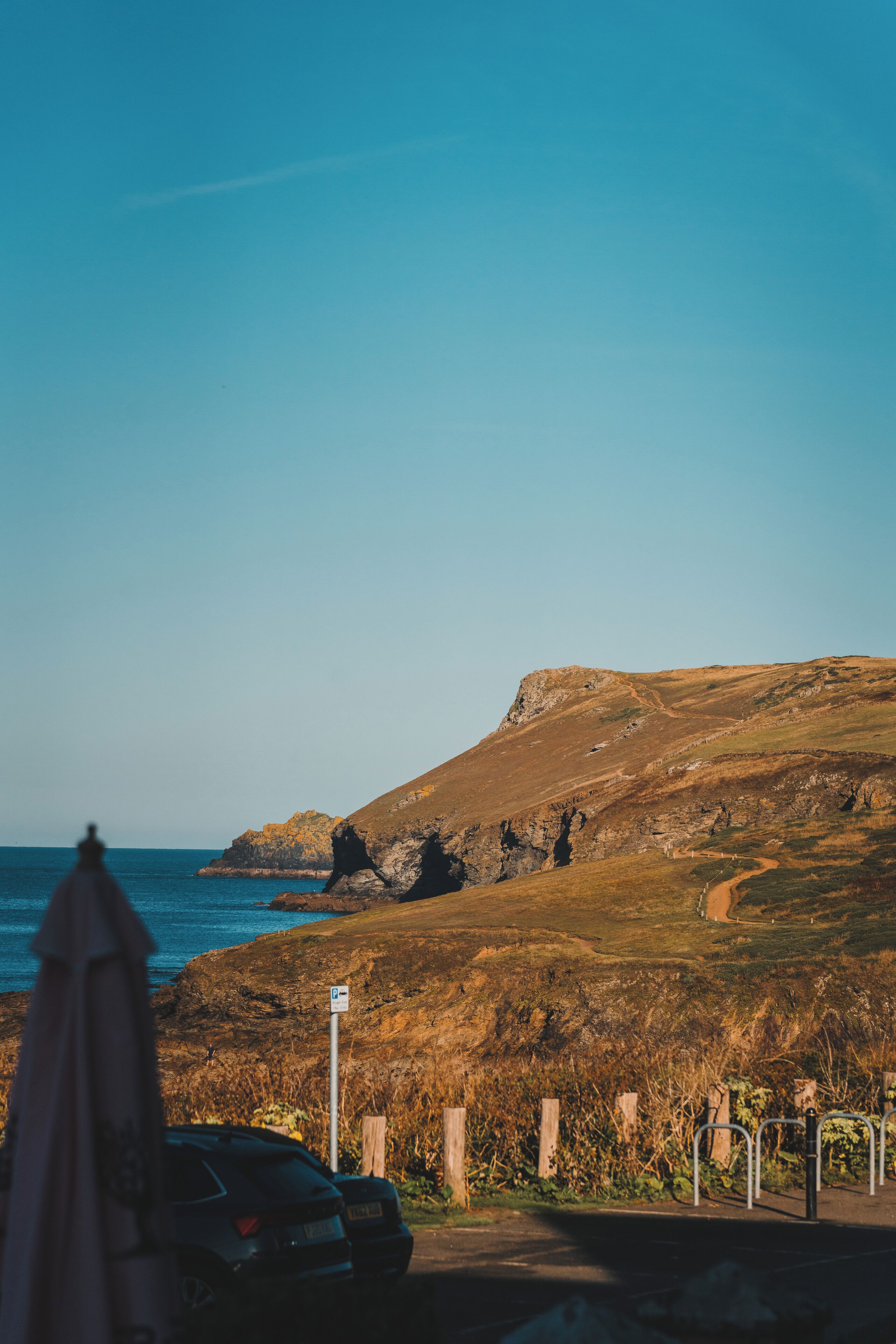 A coastal road with a parked car, a clear sky, and a rocky hill in the background.