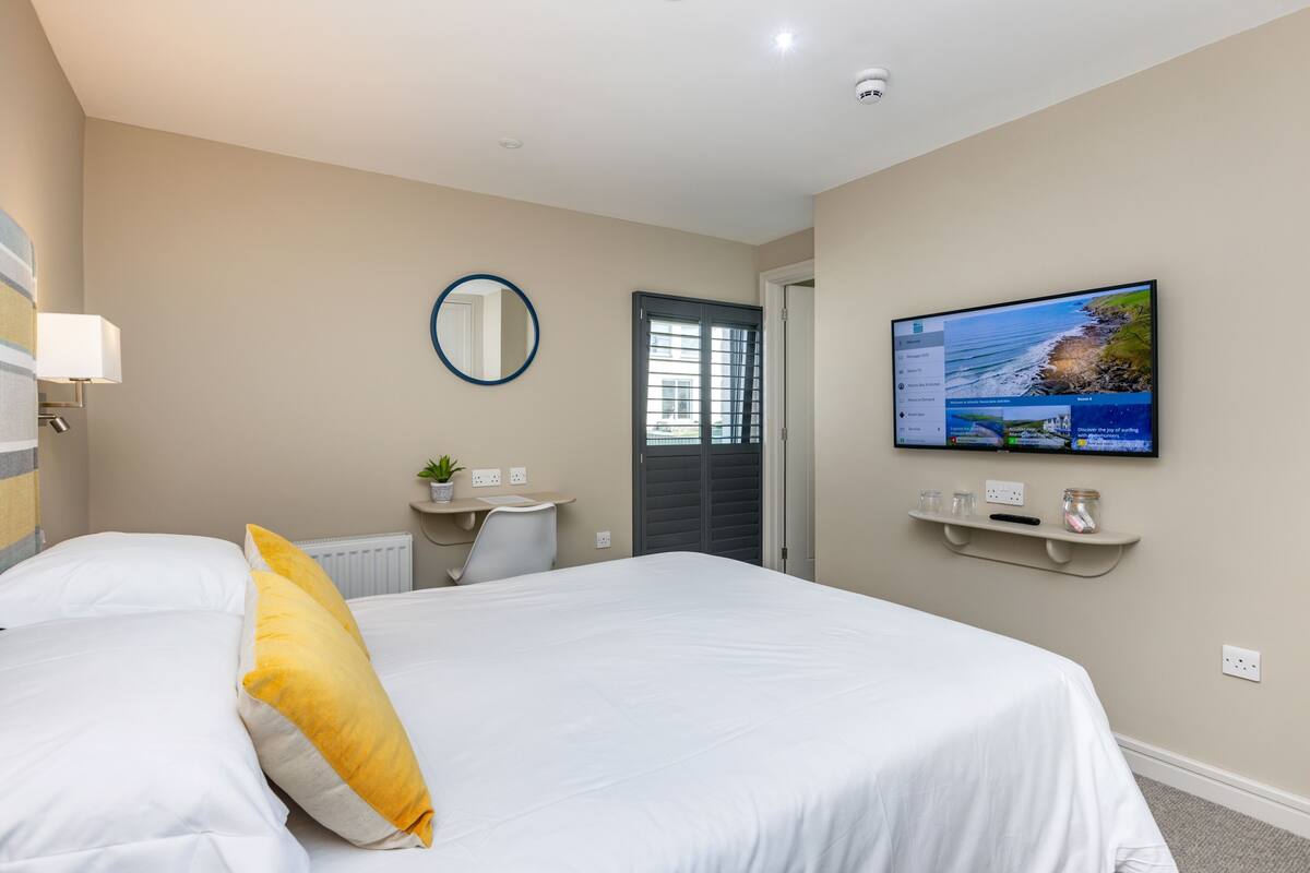 A hotel room with a bed, a desk, a chair, a television, and a window with blinds.