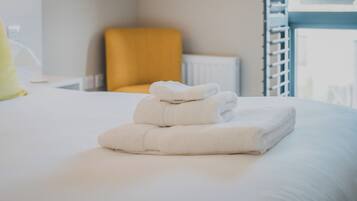 A neatly made bed with folded white towels and a yellow chair in the background.