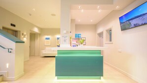 A reception area with a teal counter, a white sofa, and a large TV on the wall. - Polzeath Beach House (Wadebridge)