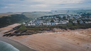 An aerial view of a coastal town with houses on a hillside, a sandy beach, and rocky cliffs. - Polzeath Beach House (Wadebridge)