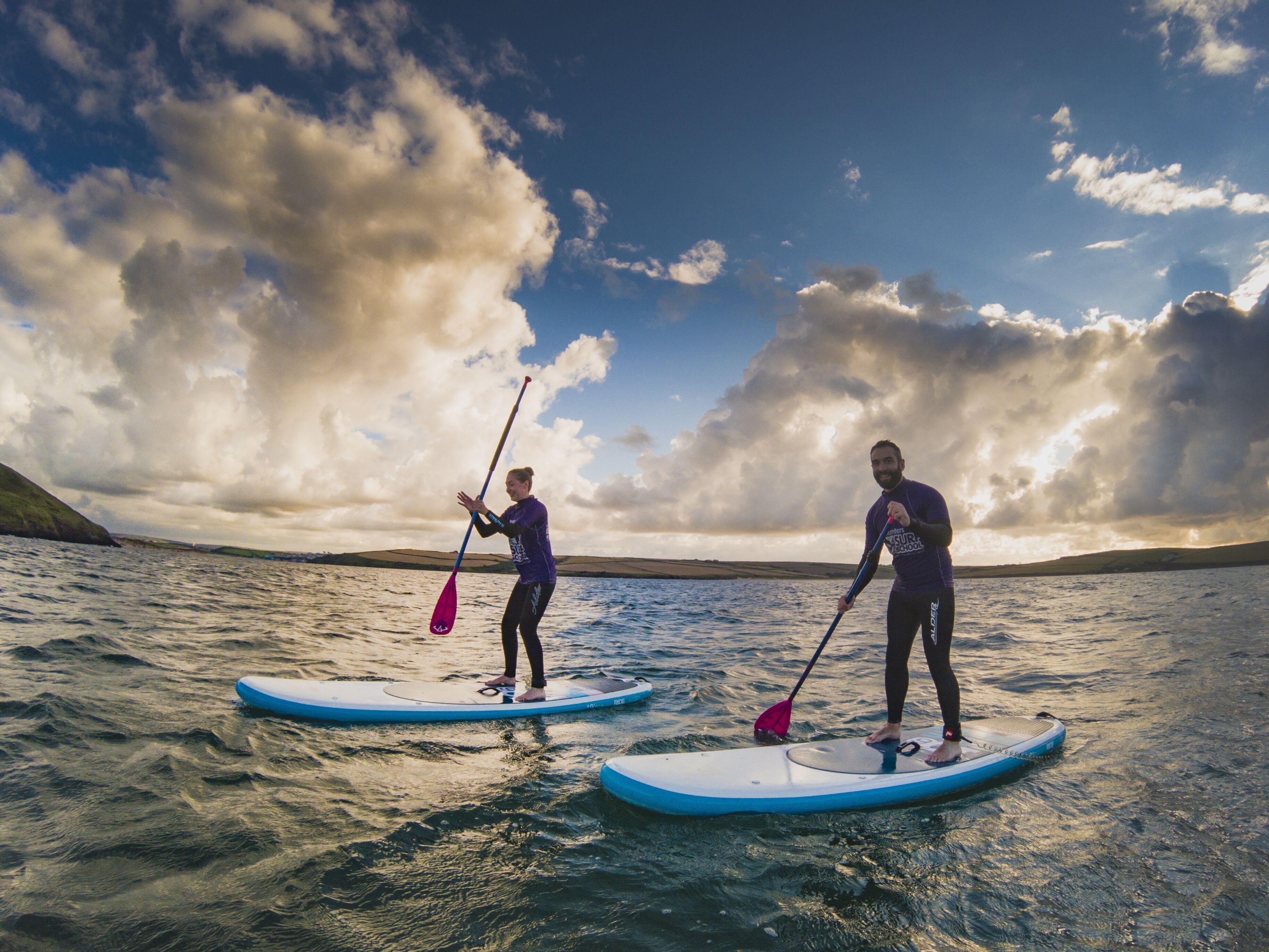 Two people on paddleboards in a body of water with a cloudy sky.