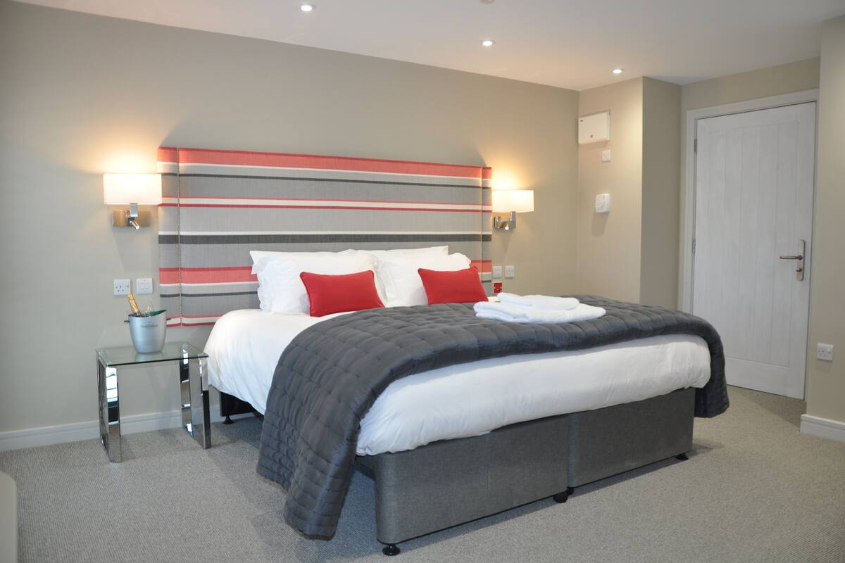 A modern hotel room with a large bed, bedside lamps, a small table, and a door.