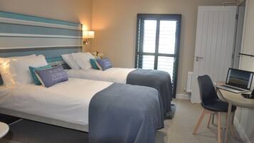 A hotel room with two beds, a desk with a laptop, a chair, and a window with blinds.