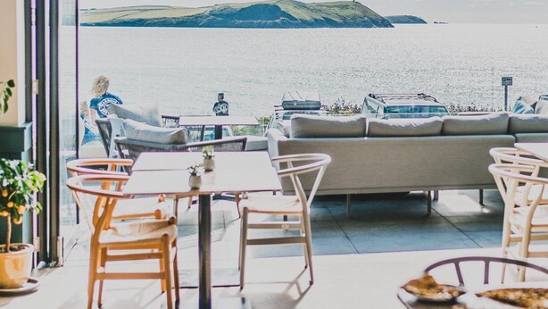 A modern outdoor dining area with a view of the sea and hills. - Polzeath Beach House (Wadebridge)