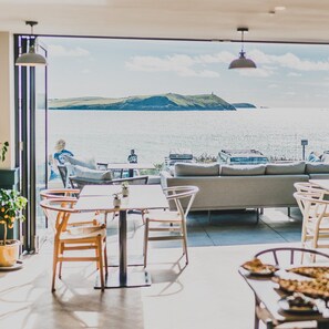A modern outdoor dining area with a view of the sea and hills. - Polzeath Beach House (Wadebridge)