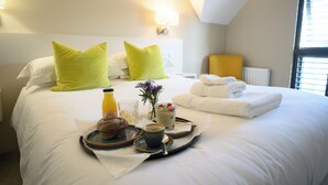 A neatly made bed with bright green pillows, a tray with breakfast items, and a bedside table with a lamp. - Polzeath Beach House (Wadebridge)