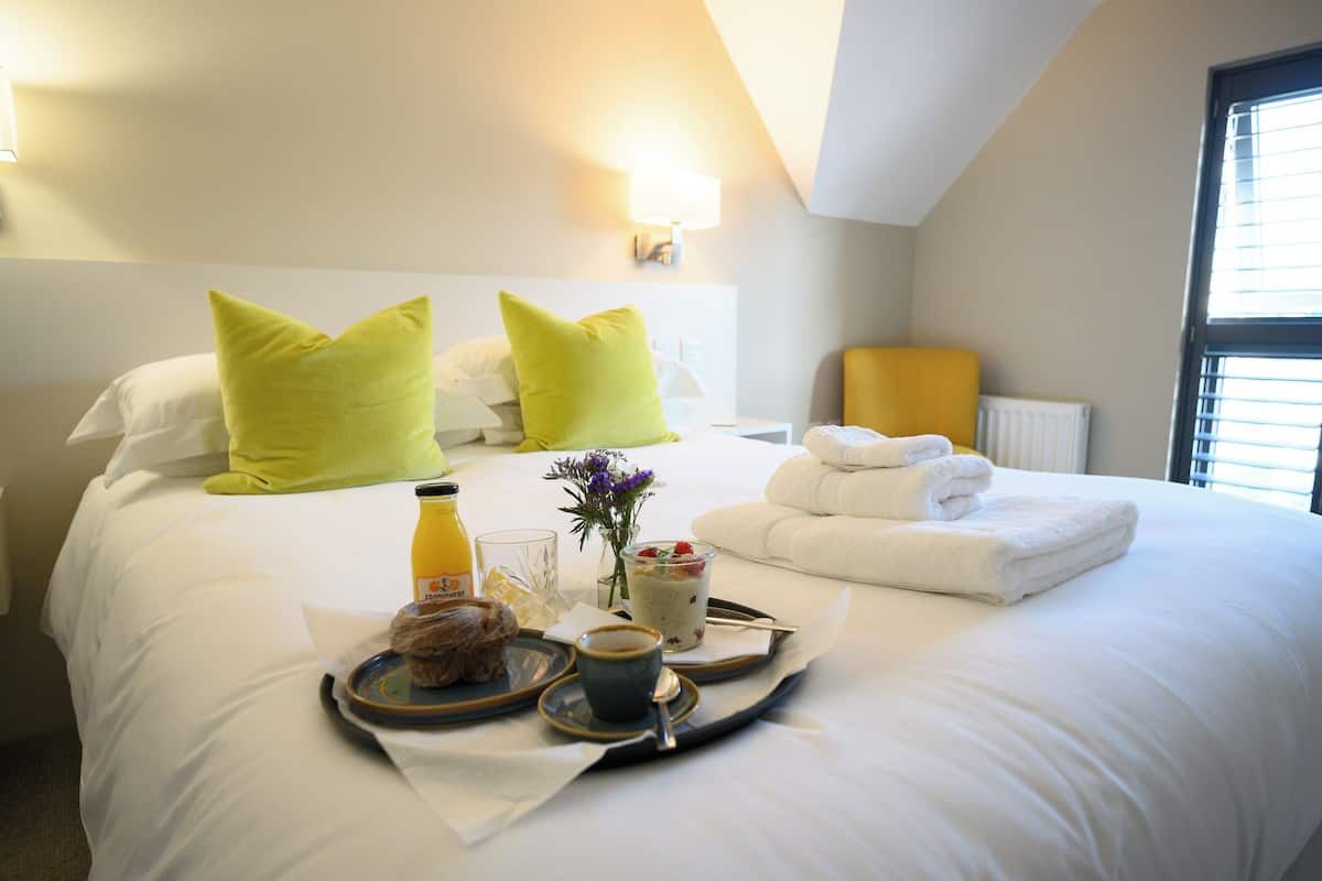 A neatly made bed with bright green pillows, a tray with breakfast items, and a bedside table with a lamp.