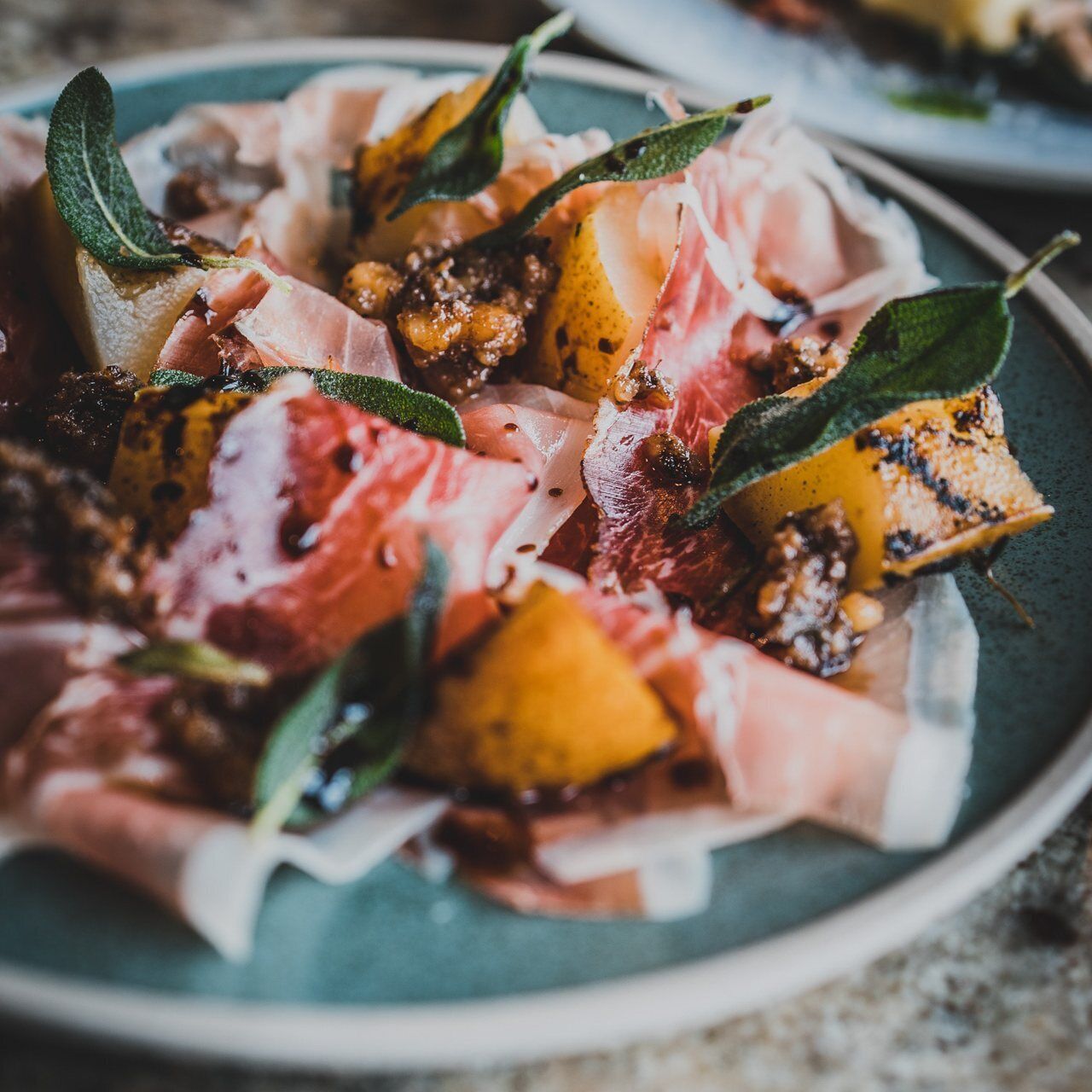 Une assiette de nourriture comprenant du jambon de Parme, des figues et des feuilles de sauge.
