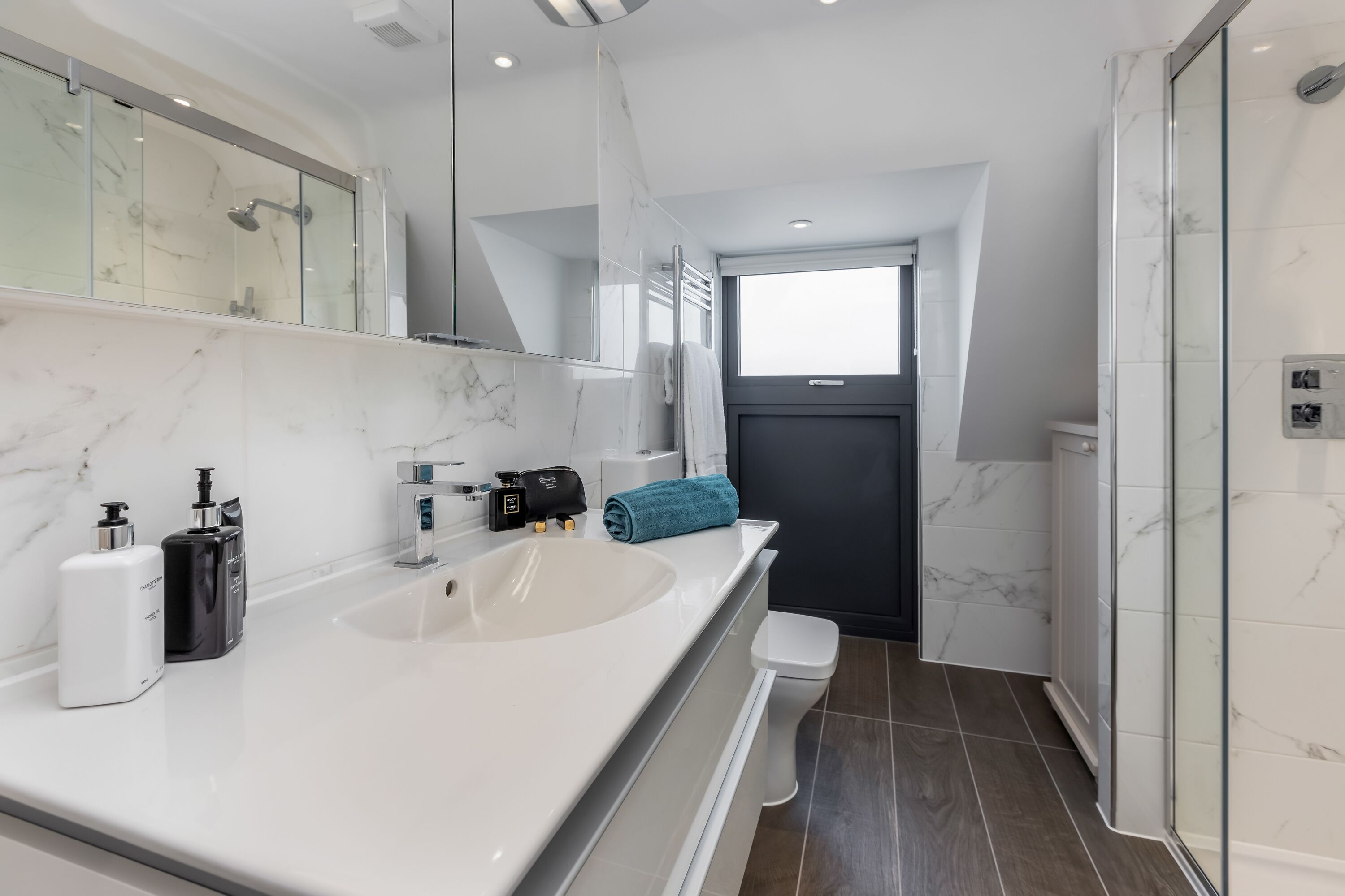 Un baño moderno con un lavamanos grande y blanco, cabina de ducha de vidrio y una puerta oscura.