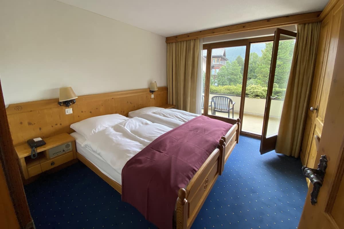 Habitación de hotel con una cama doble, una mesita de noche con lámpara, una silla junto a la ventana y vistas al exterior.