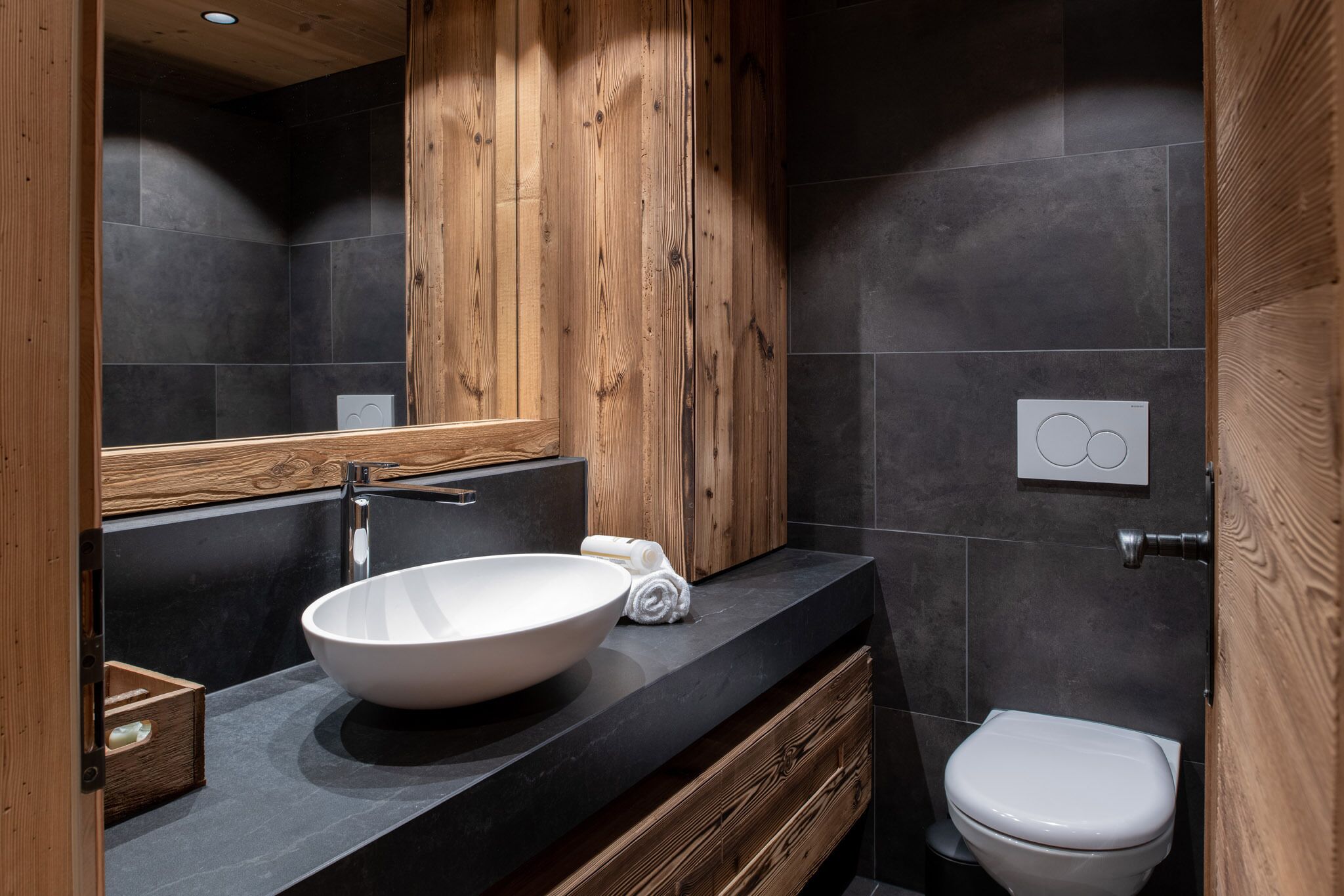 A modern bathroom with a wooden vanity, a large white sink, and a white toilet.