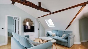 Un salon moderne de style « loft », avec des poutres apparentes en bois, une grande fenêtre et un ensemble de canapés bleus.