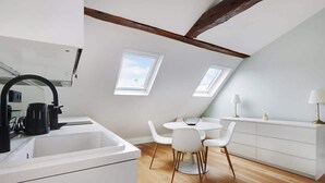 Une cuisine moderne avec un plan de travail blanc, une machine à café et un évier. Elle est dotée de deux puits de lumière et comprend un coin repas avec une table ronde et des chaises blanches.