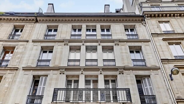Un immeuble à plusieurs étages, de style architectural classique, doté de balcons avec des garde-corps en fer forgé et de grandes fenêtres.