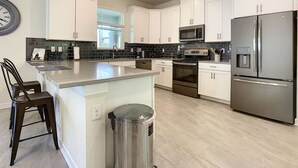 Una cocina moderna con gabinetes blancos, electrodomésticos de acero inoxidable y una isla central con taburetes de bar.