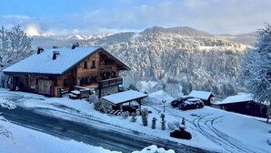 Una cabaña de madera con balcón, rodeada de árboles y montañas cubiertas de nieve.