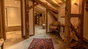 Un interior rústico con vigas de madera a la vista, una alfombra estampada y una silla junto a una mesita.