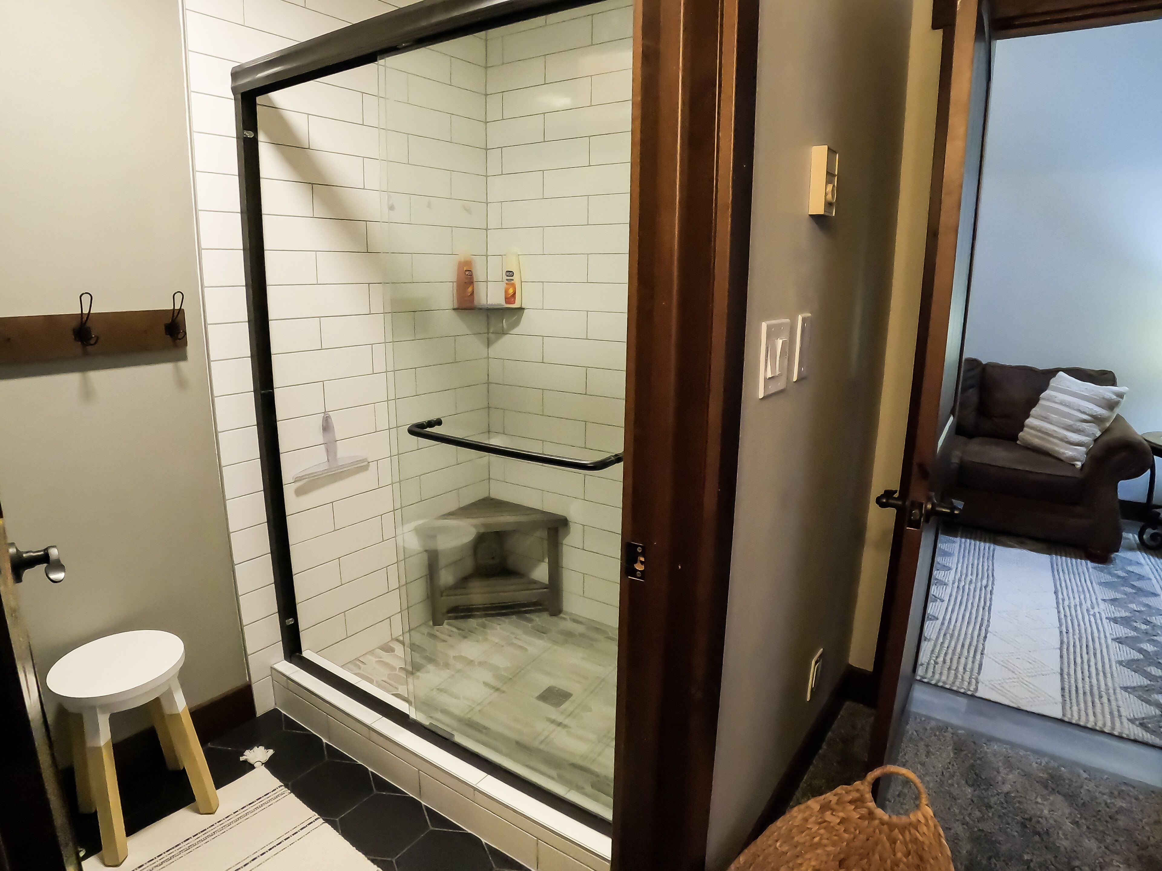 A modern bathroom with a glass-enclosed shower, a white toilet, and a small stool.