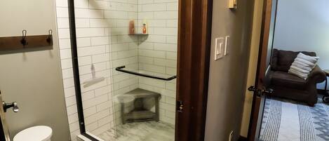 A modern bathroom with a glass-enclosed shower, a white toilet, and a small stool.