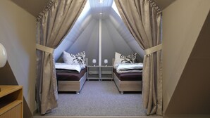 Une chambre avec deux lits, une commode en bois et une lucarne.