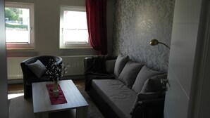 Un salon comprenant un canapé, une table basse, un fauteuil, une fenêtre avec des rideaux et un mur à motifs.