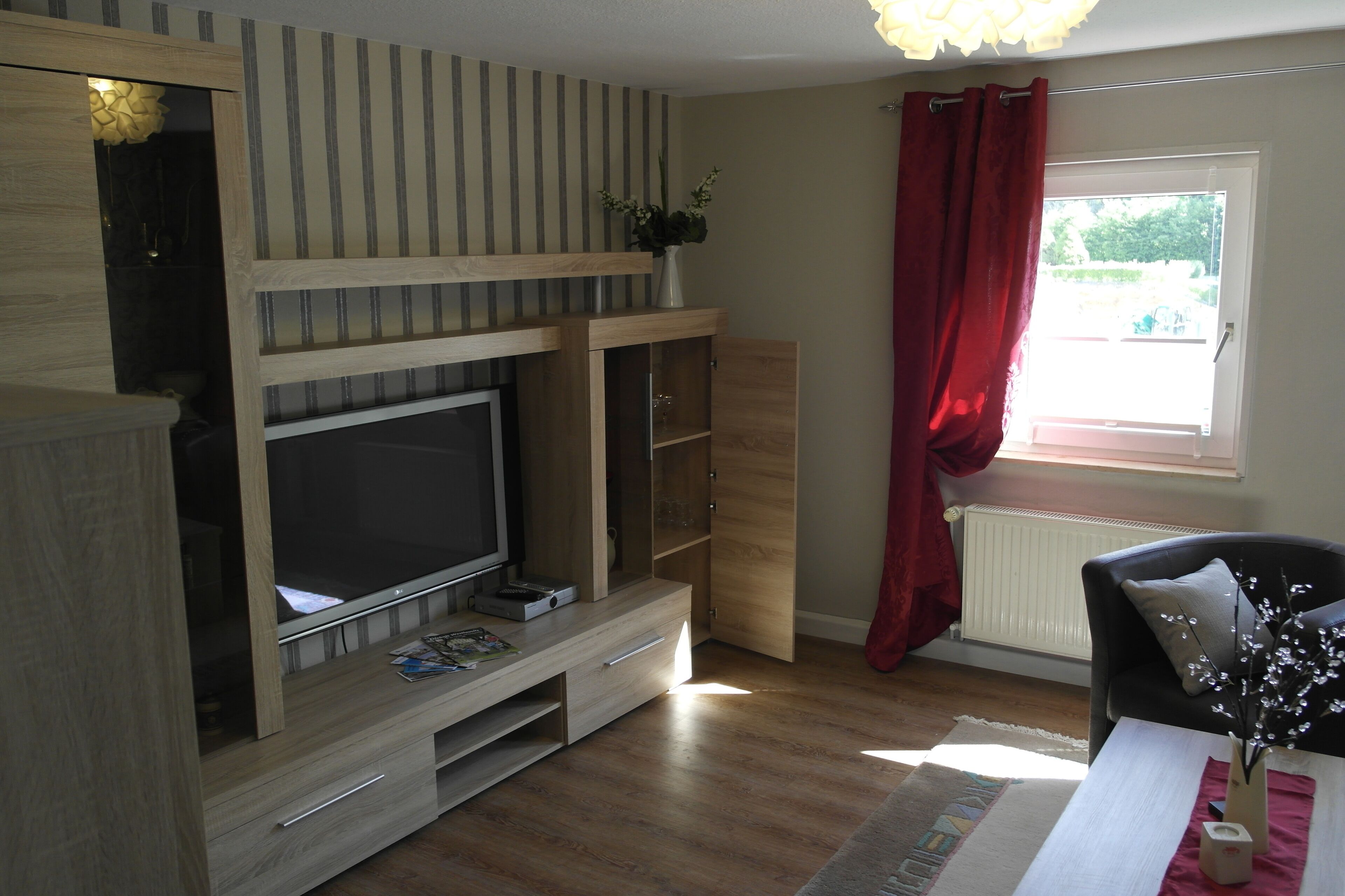 Ein Wohnzimmer mit einer Holzunterhaltungsecke, einem Flachbildfernseher und einem Fenster mit roten Vorhängen.