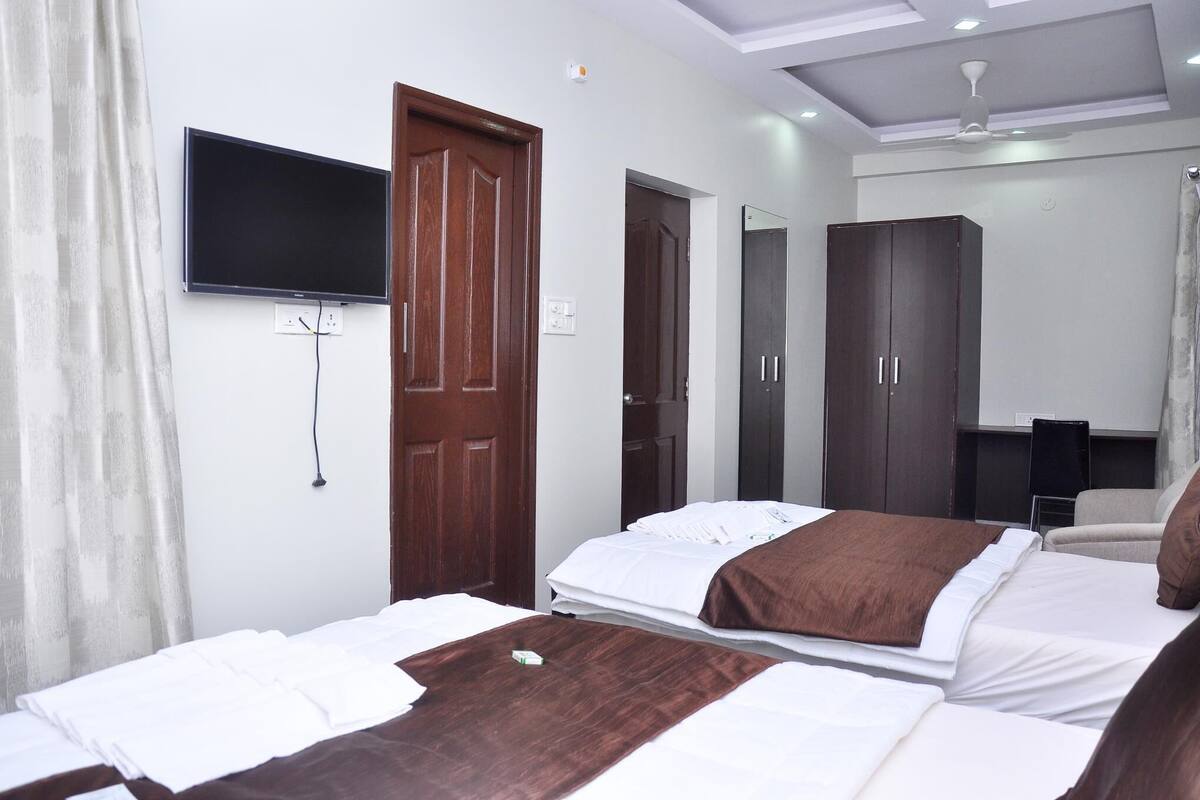 A hotel room with two beds, a TV mounted on the wall, a wardrobe, and a ceiling fan.