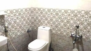 A small bathroom with a toilet, a sink, and a shower. The walls are tiled with a circular pattern. - PPH Living GS Suites (Bengaluru)