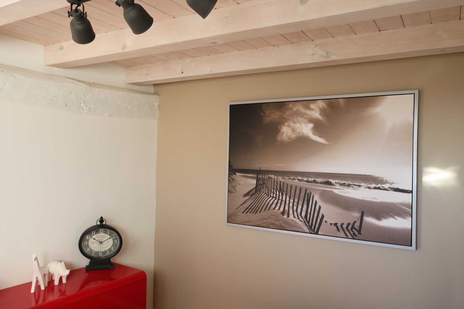 Una habitación con techo de madera, un armario rojo, un reloj en la pared y una fotografía enmarcada de una playa.