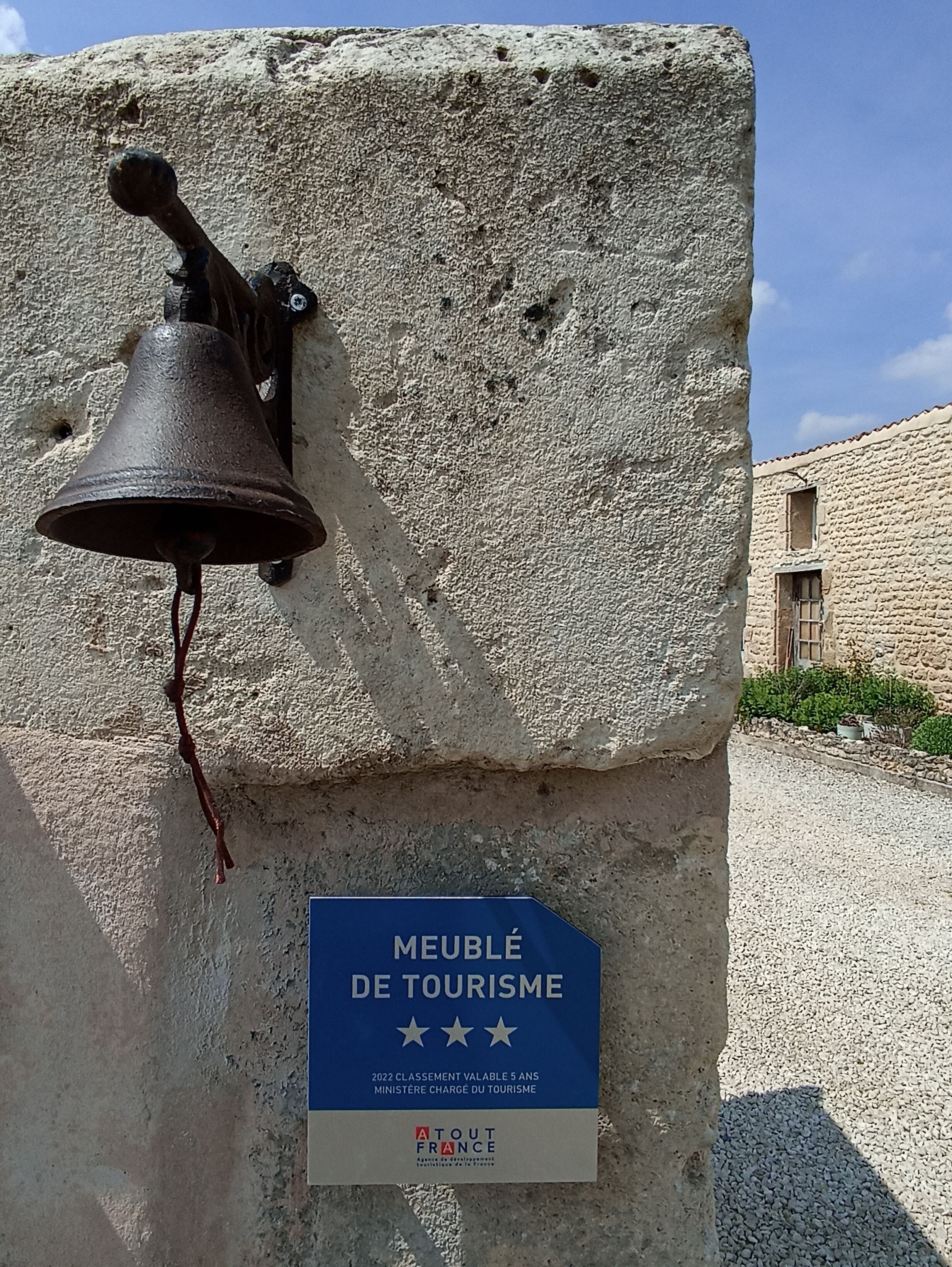 Une construction en pierre surmontée d’une cloche et d’un panneau bleu indiquant qu’il s’agit d’un site touristique.