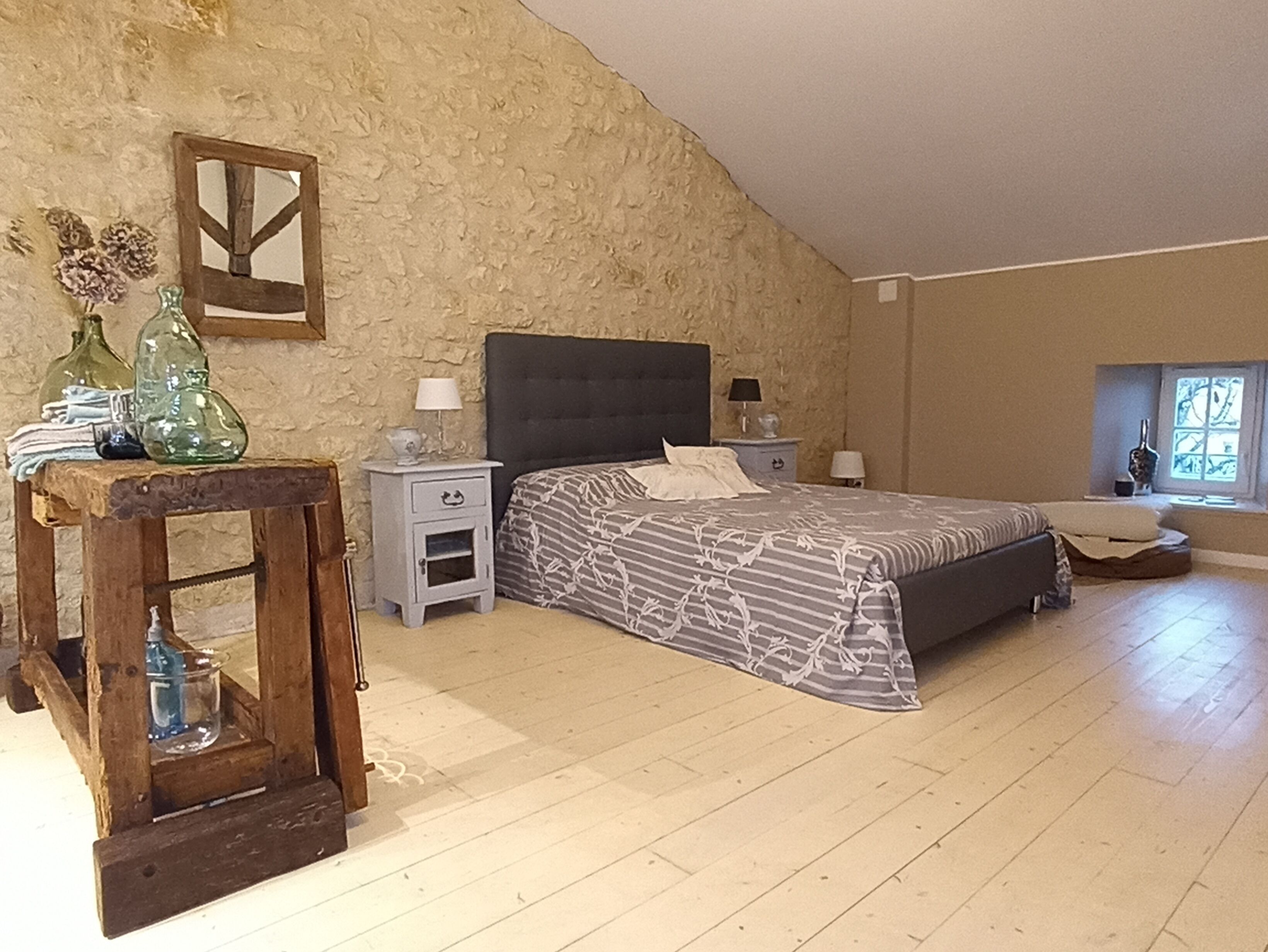 A bedroom with a bed, nightstands, a wooden table, and a stone wall.