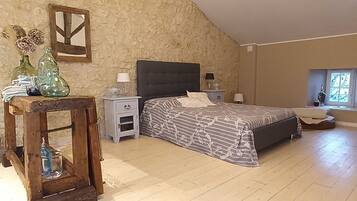 A bedroom with a bed, nightstands, a wooden table, and a stone wall.