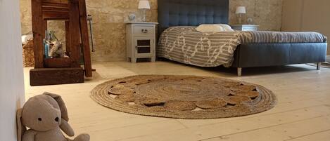 Una camera da letto con parete in pietra, un letto con copripiumino decorato, un comodino in legno, un tavolino da notte con lampade e un tappeto intrecciato.