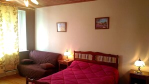 A bedroom with a wooden bed, a wooden chair, two bedside tables with lamps, a window with floral curtains, and two framed pictures on the wall. - Country house 5 min from lake genin (Charix)
