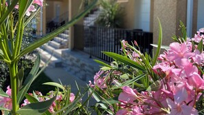 A building with balconies, a staircase, and a garden with pink flowers. - Superb T3 N°1 Garden level Apartment, swimming pool, terrace (bastia)