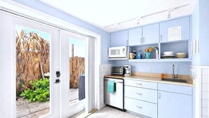 A compact kitchen with a microwave, toaster, and sink, featuring light blue cabinets and a view through a glass door. - Waterfront-20 Steps to Private Beach-1+ BR-Pets OK-Kayaks-SUPs-Best Sharkteeth (Englewood)