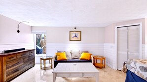 A room with a wooden dresser, a white table, a sofa with yellow cushions, a framed picture on the wall, and a closed closet. - Waterfront-20 Steps to Private Beach-1+ BR-Pets OK-Kayaks-SUPs-Best Sharkteeth (Englewood)