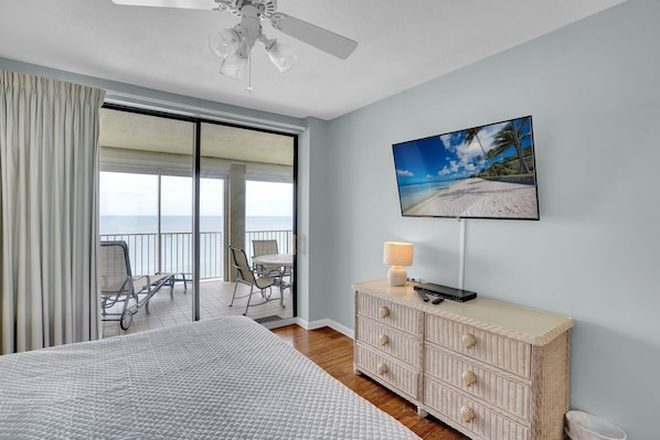 A hotel room with a bed, a television, a wicker dresser, and a balcony with a view of the beach.