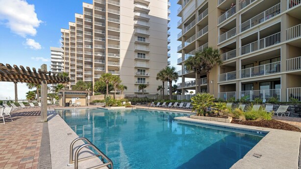 A swimming pool with lounge chairs and a pergola, surrounded by tall residential buildings. - White Caps 1506 by Liquid Life (Orange Beach)