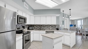 A modern kitchen with a central island, stainless steel appliances, and a tiled backsplash. - White Caps 1506 by Liquid Life (Orange Beach)