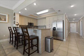 A modern kitchen with white cabinets, a stainless steel refrigerator, and a central island with bar stools.