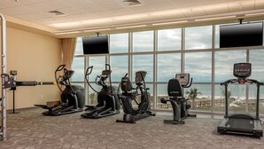 Ein Fitnessstudio mit verschiedenen Cardiogeräten, großen Fenstern und Blick auf den Strand.