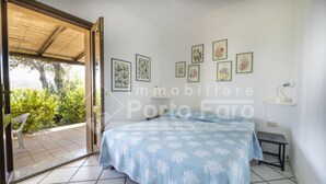 Ein Schlafzimmer mit Bett, einem kleinen Nachttisch, einem Sessel und Blick ins Freie.