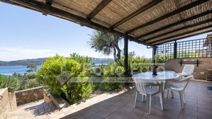 Eine überdachte Terrasse mit Tisch und Stühlen, mit Blick auf eine malerische Seen- und Hügellandschaft.