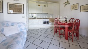 Ein kompakter Wohnraum mit Küchenzeile, einer Essecke mit roten Stühlen und einem gemusterten Sofa.