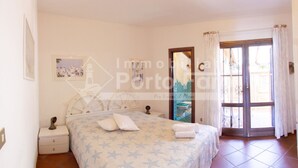 A bedroom with a bed, nightstands, a window with curtains, and a door leading outside. - 13A Appartamento - 13A PORTO MANNU (Palau)
