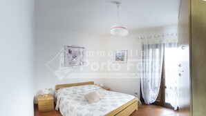 A bedroom with a bed, a bedside table, a hanging light fixture, and a window with curtains. - 15B Appartamento - 15B PORTO MANNU (Palau)